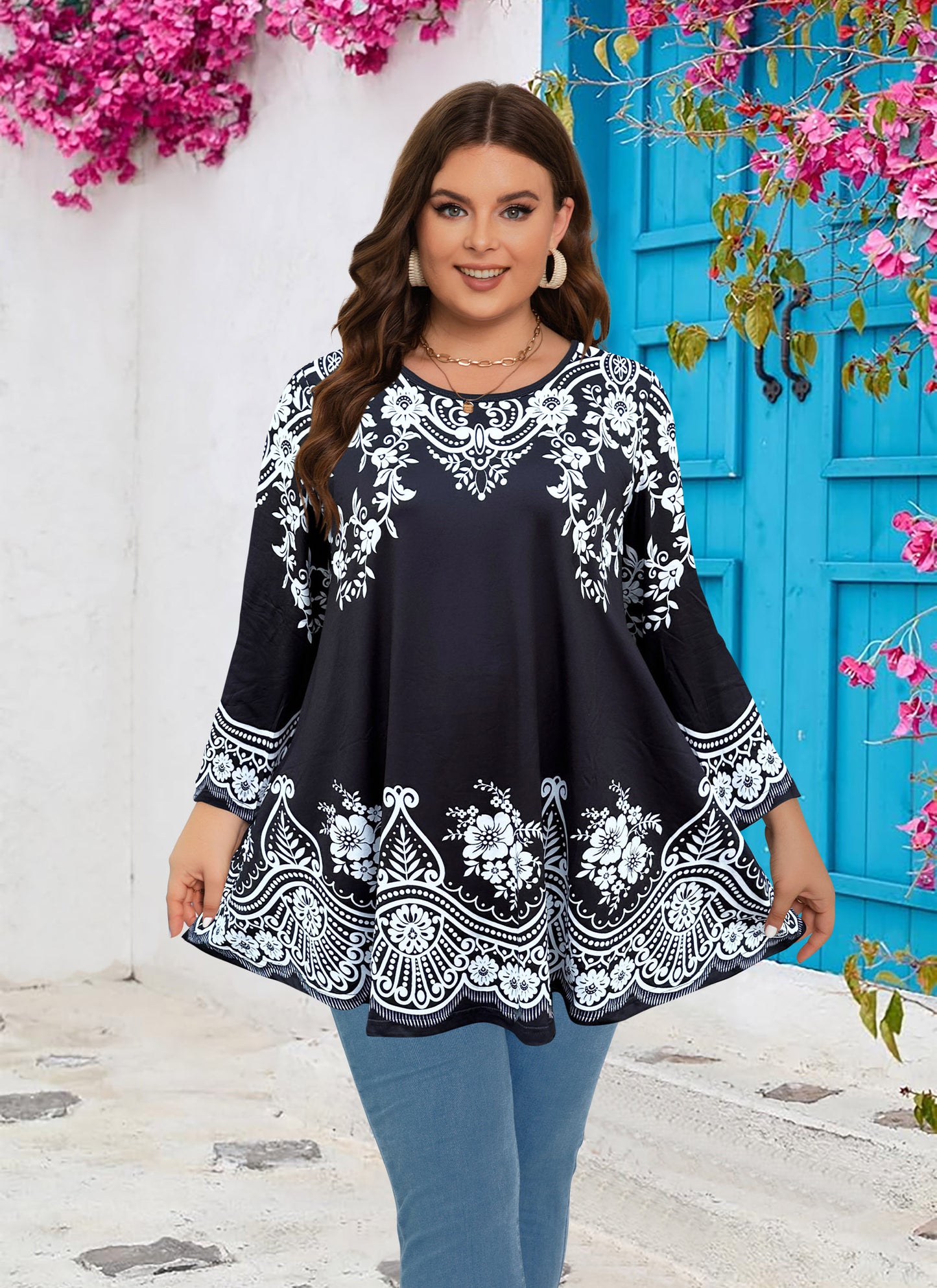 Woman wearing a black and white patterned dress with a blue door and pink flowers in the background