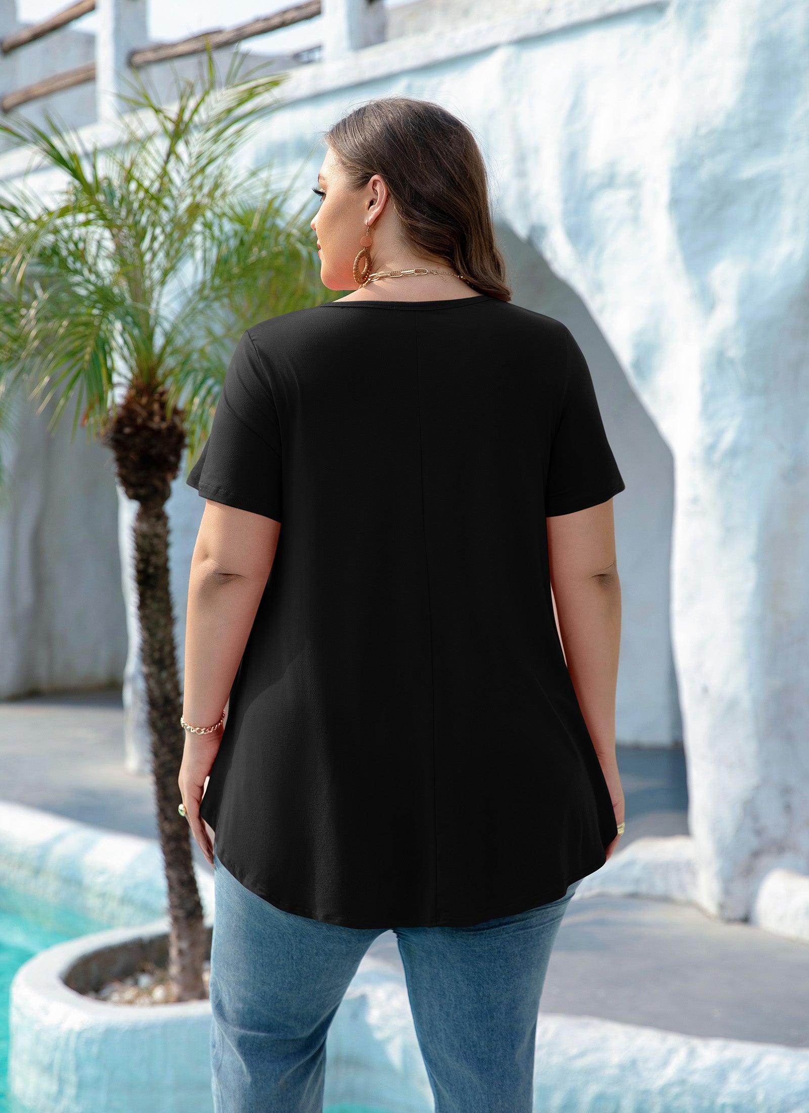 Woman wearing a black t-shirt and blue jeans standing by a pool with palm trees in the background.