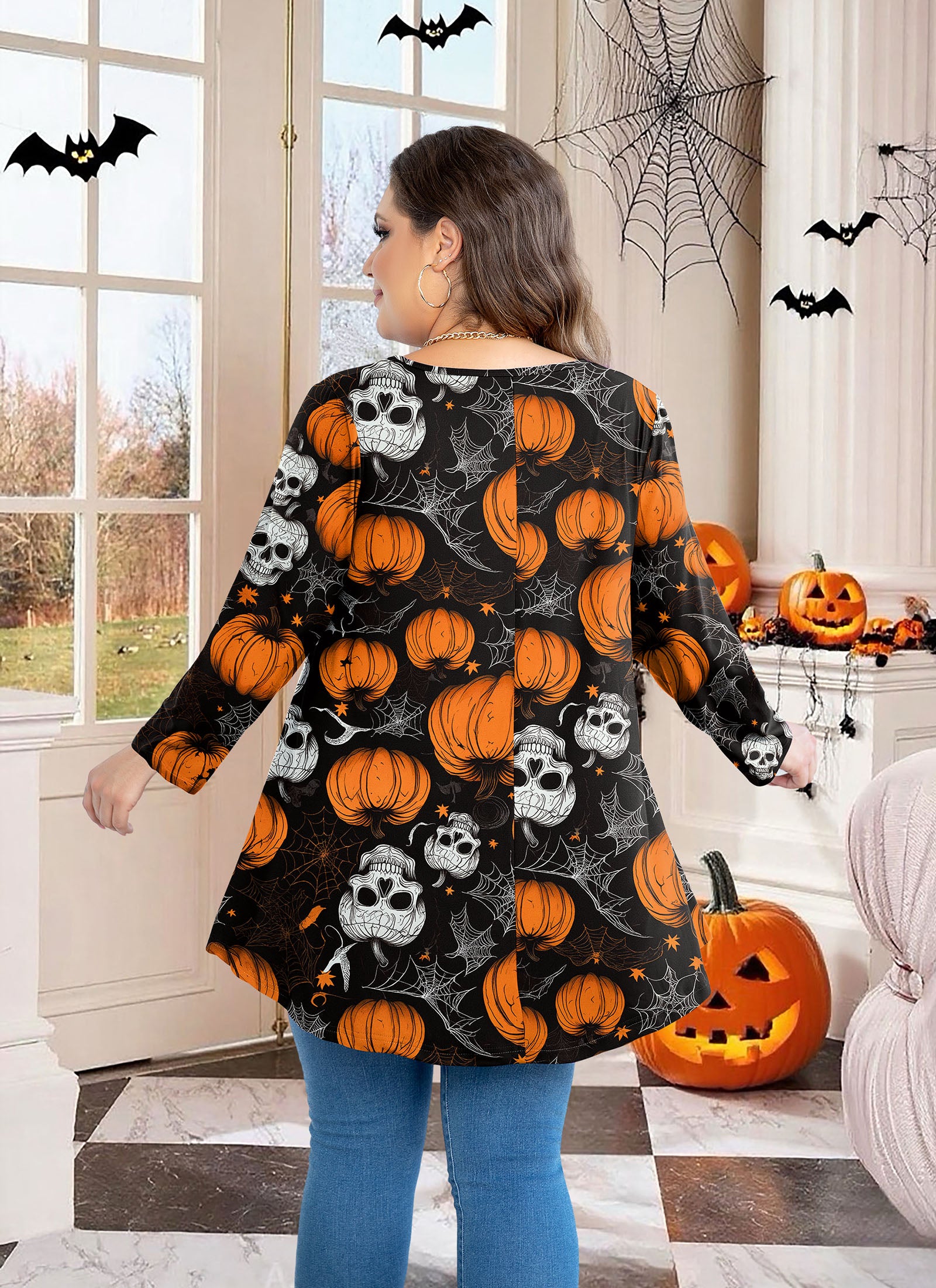 Woman wearing a Halloween-themed sweater with pumpkins and skulls in a decorated room.